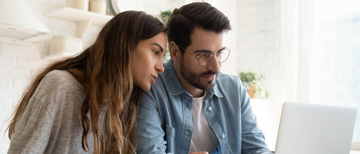 Focused young couple calculating bills, discussing planning budget together, serious wife and husband looking at laptop screen, using online banking services and calculator, checking finances