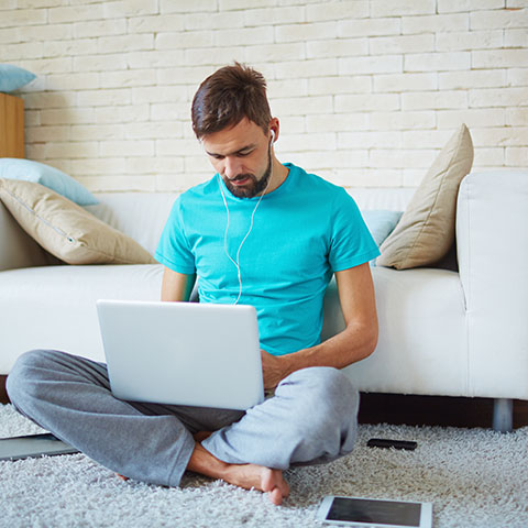 Guy in blue shirt sitting cris cross looking at laptop
